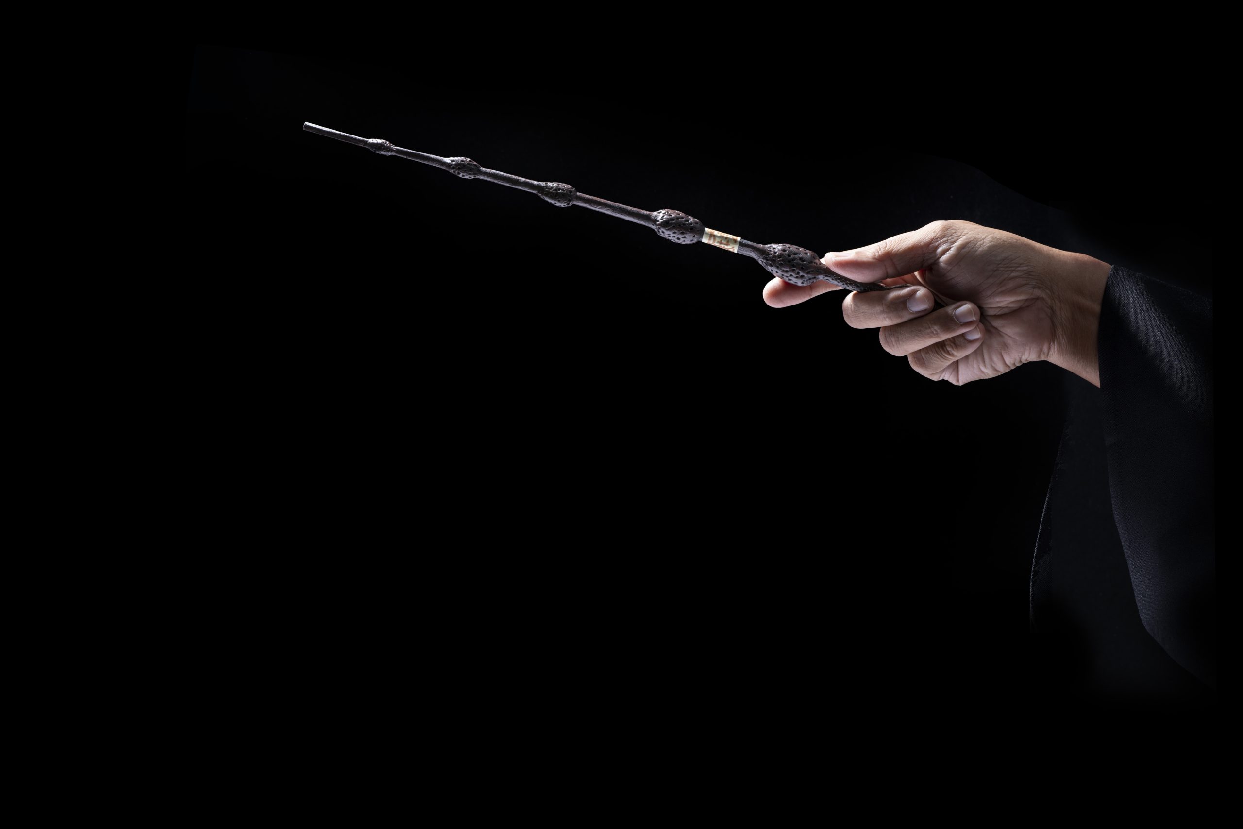 A hand holding a magic wand on the dark background.