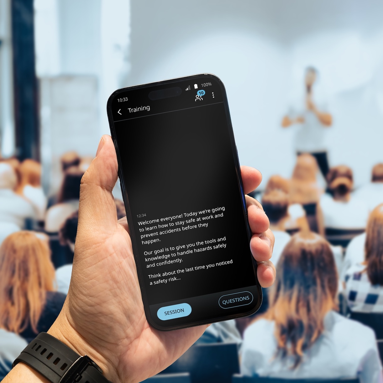 В залата, пълна с хора, се провежда лекция. Мъжът държи в ръка телефона си, на който се показва преводът чрез Vasco Audience