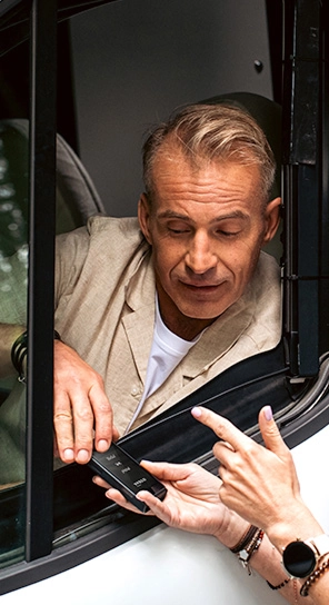 Мъж, седнал в кола, говори с устройството Vasco Q1, което някой му подава.