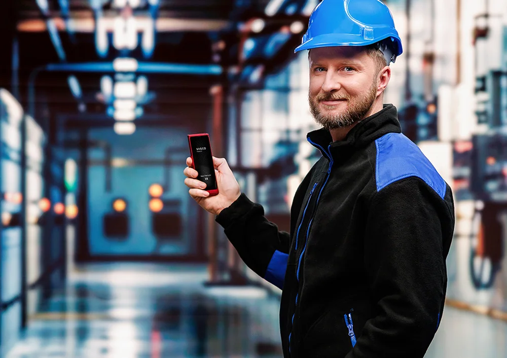 Шофьор на камион пред камиона си, държащ документи в едната ръка и Vasco Translator V4 в другата, като на екрана на устройството се вижда функцията за превод на снимки.