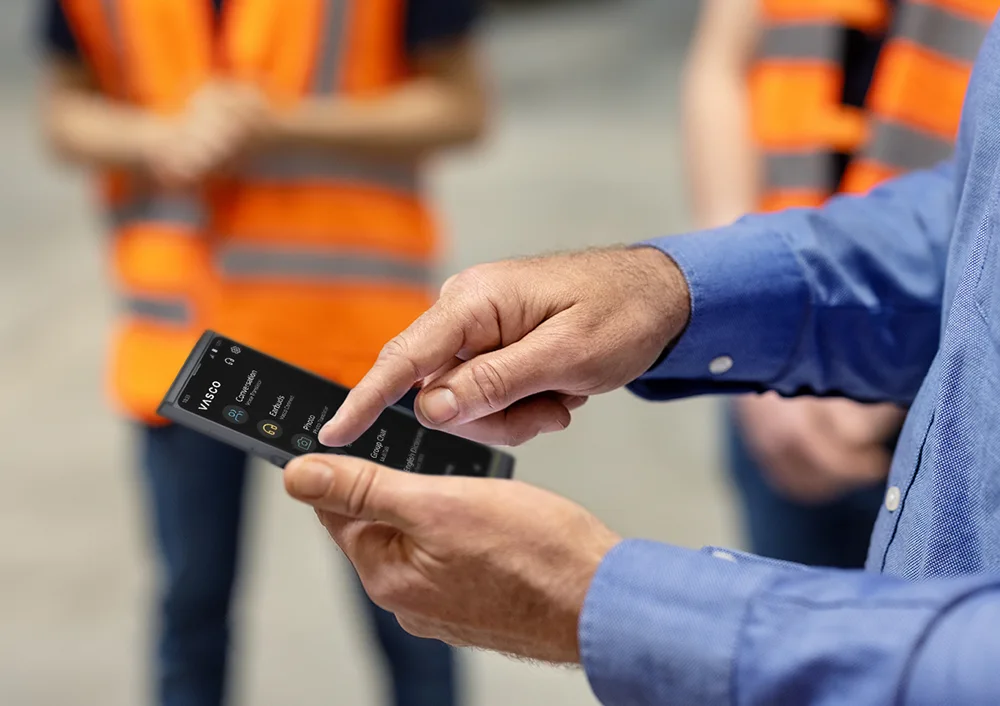 Човек, държащ Vasco V4, на фона се виждат хора в работно облекло.