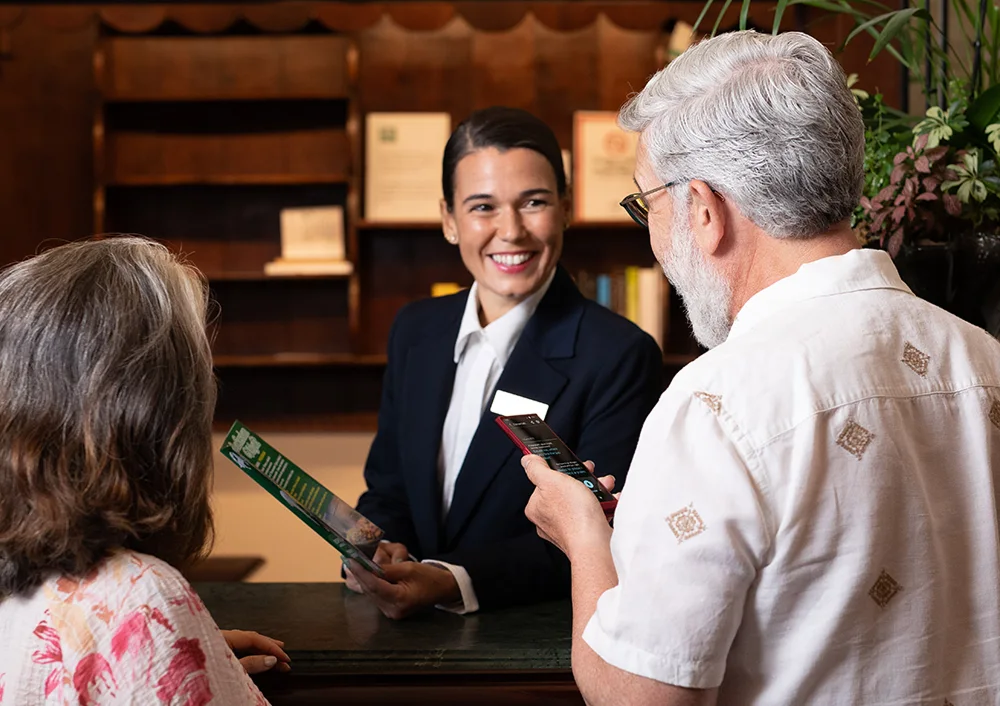 Усмихната рецепционистка, която слуша превода от Vasco Translator V4, държан от мъж и насочен към нея.