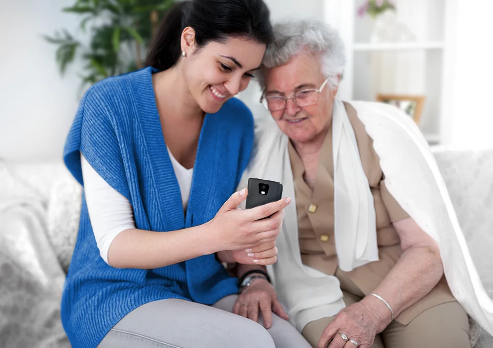 Жена показва преводач Vasco Translator Q1 на възрастна жена, демонстрирайки как той помага на възрастните хора.